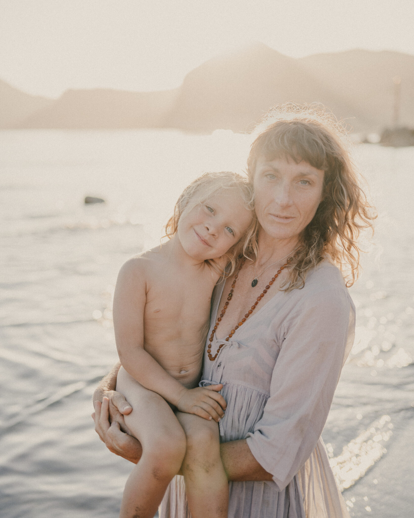 Mother holding young child beside the sea in the golden hour.