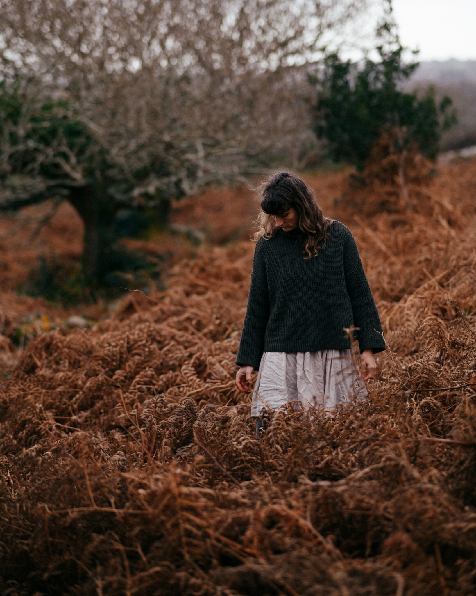Woman looking down and standing on bracken covered hillside.