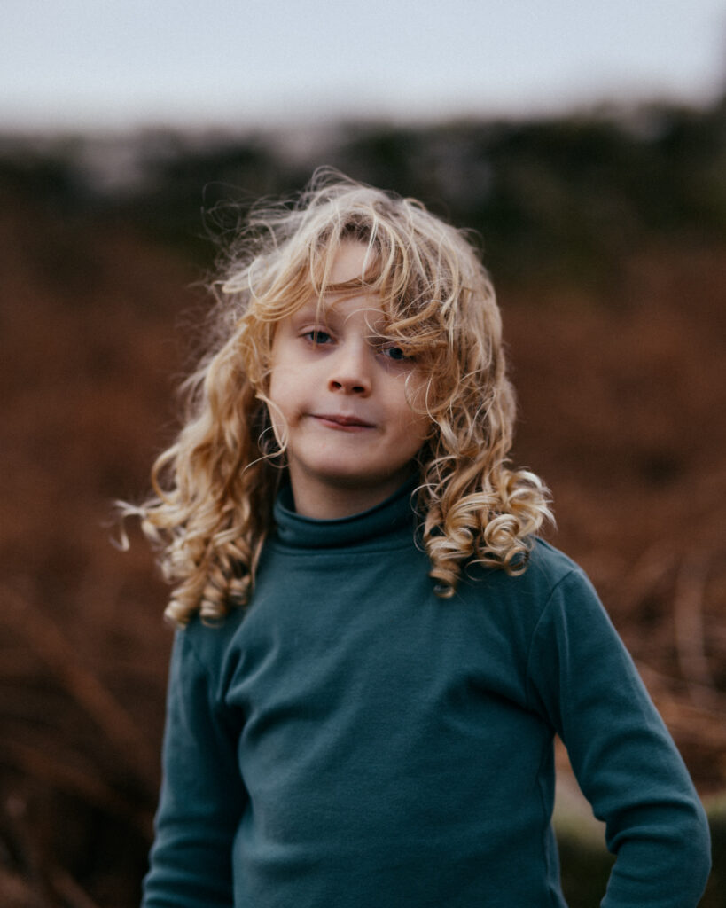 Young boy with long blonde curly hair and a green polo neck top.