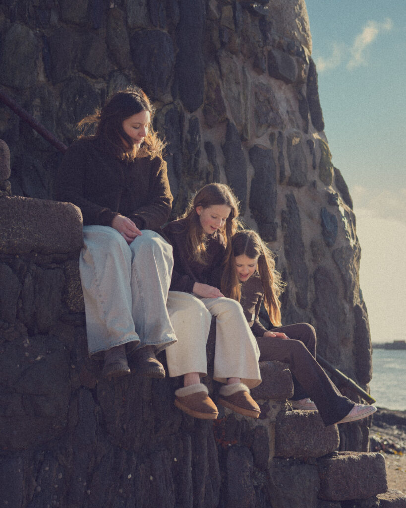 Family of three people sitting on pier steps in Cornwall.