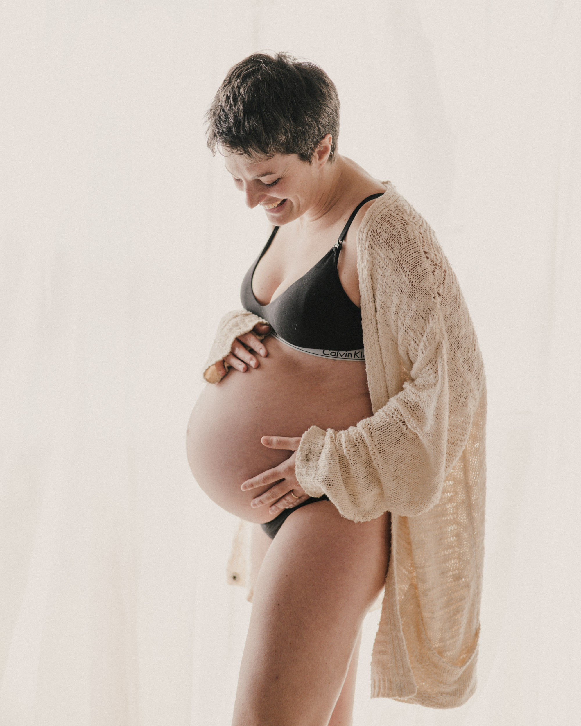 Women holding baby bump in white cardigan