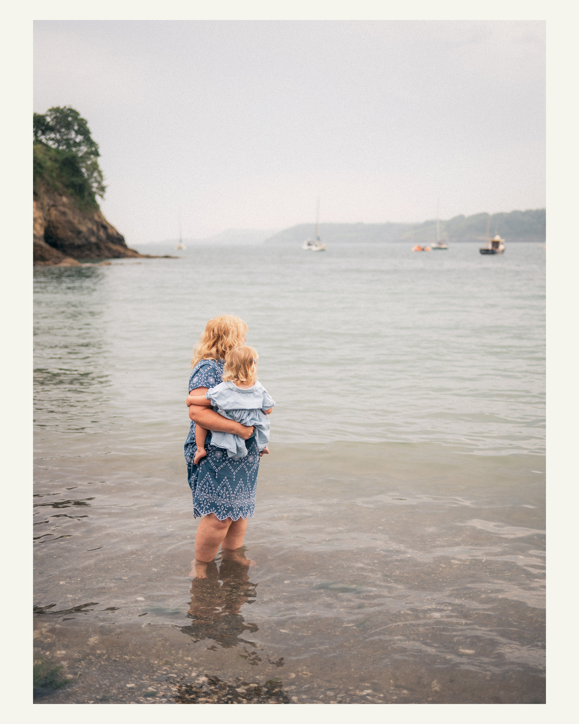 Grandmother holding her young granddaughter while standing in the water at Grebe Beach