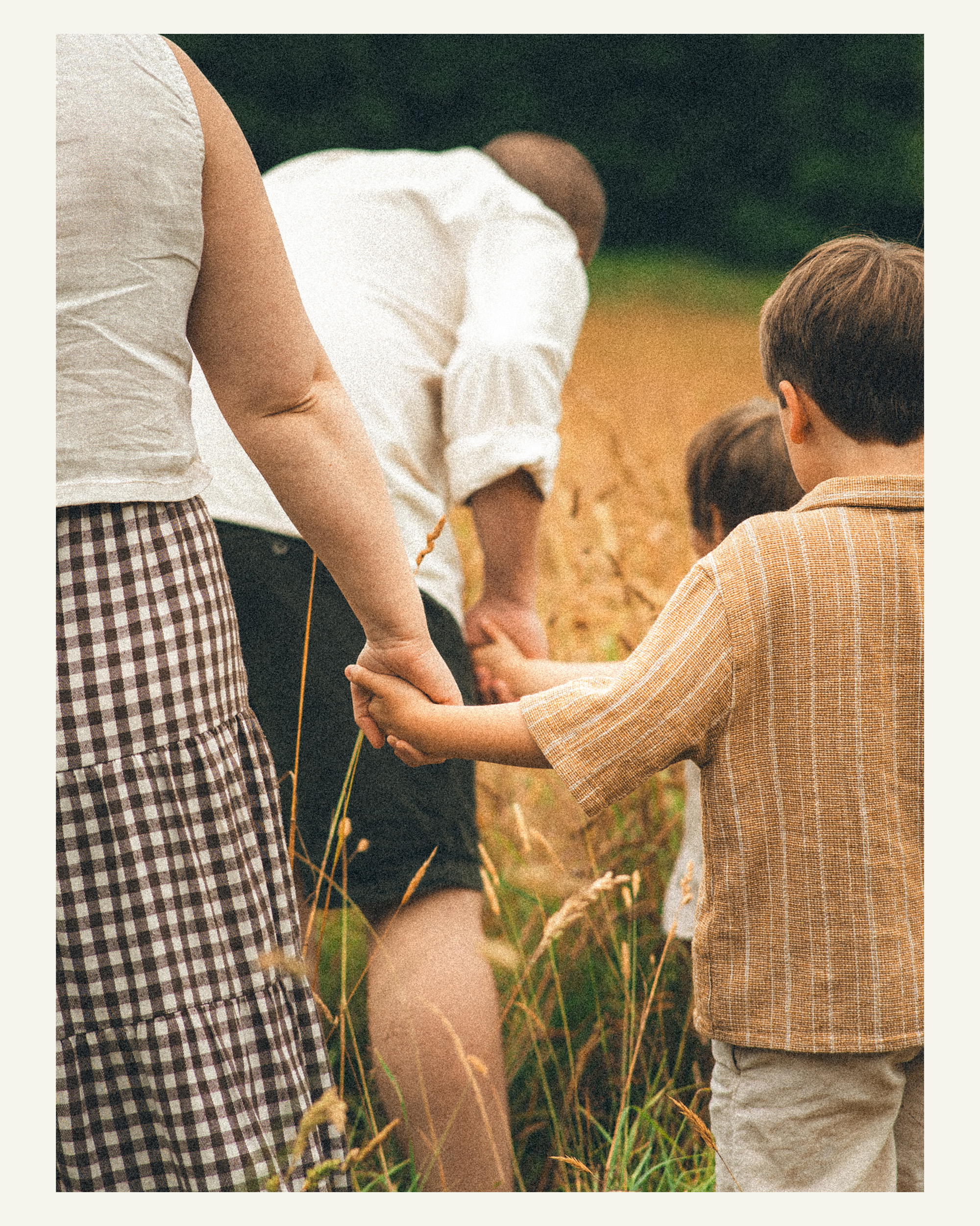 Mother holding her son’s hand as the family walks through long grass at Trelissick Gardens