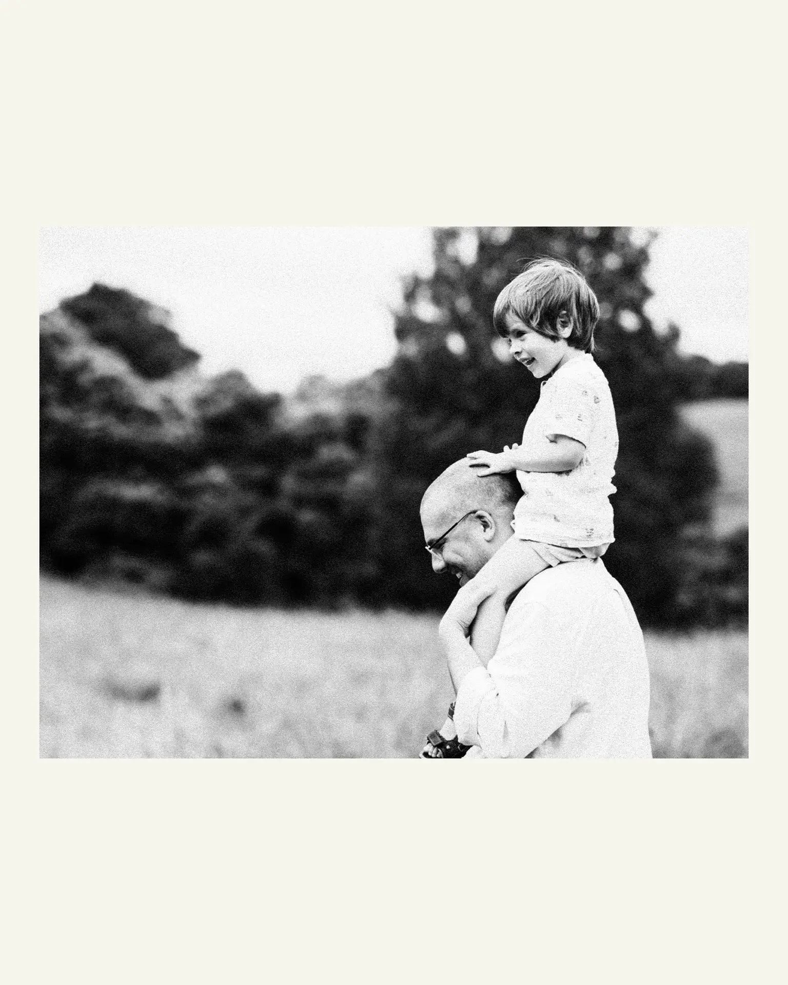 Father smiling as he carries his young son on his shoulders through a meadow at Trelissick Gardens