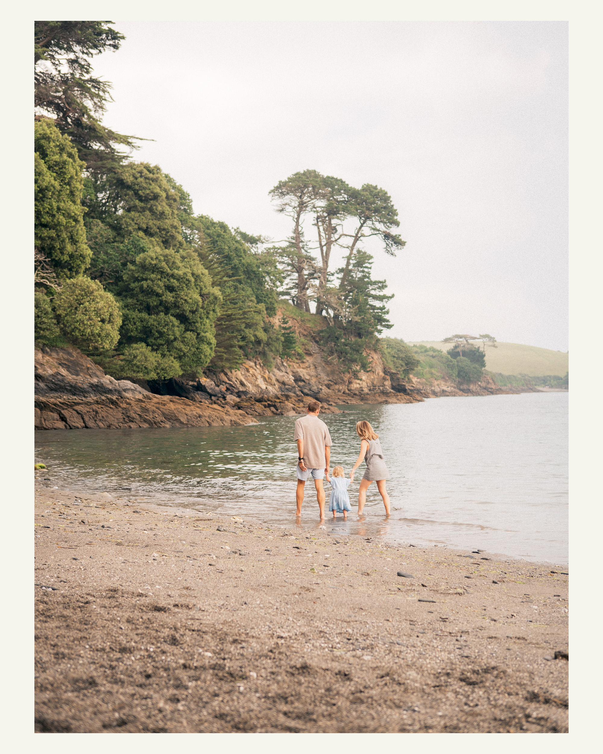 Parents holding their young daughter’s hands as they paddle at Grebe Beach near Falmouth