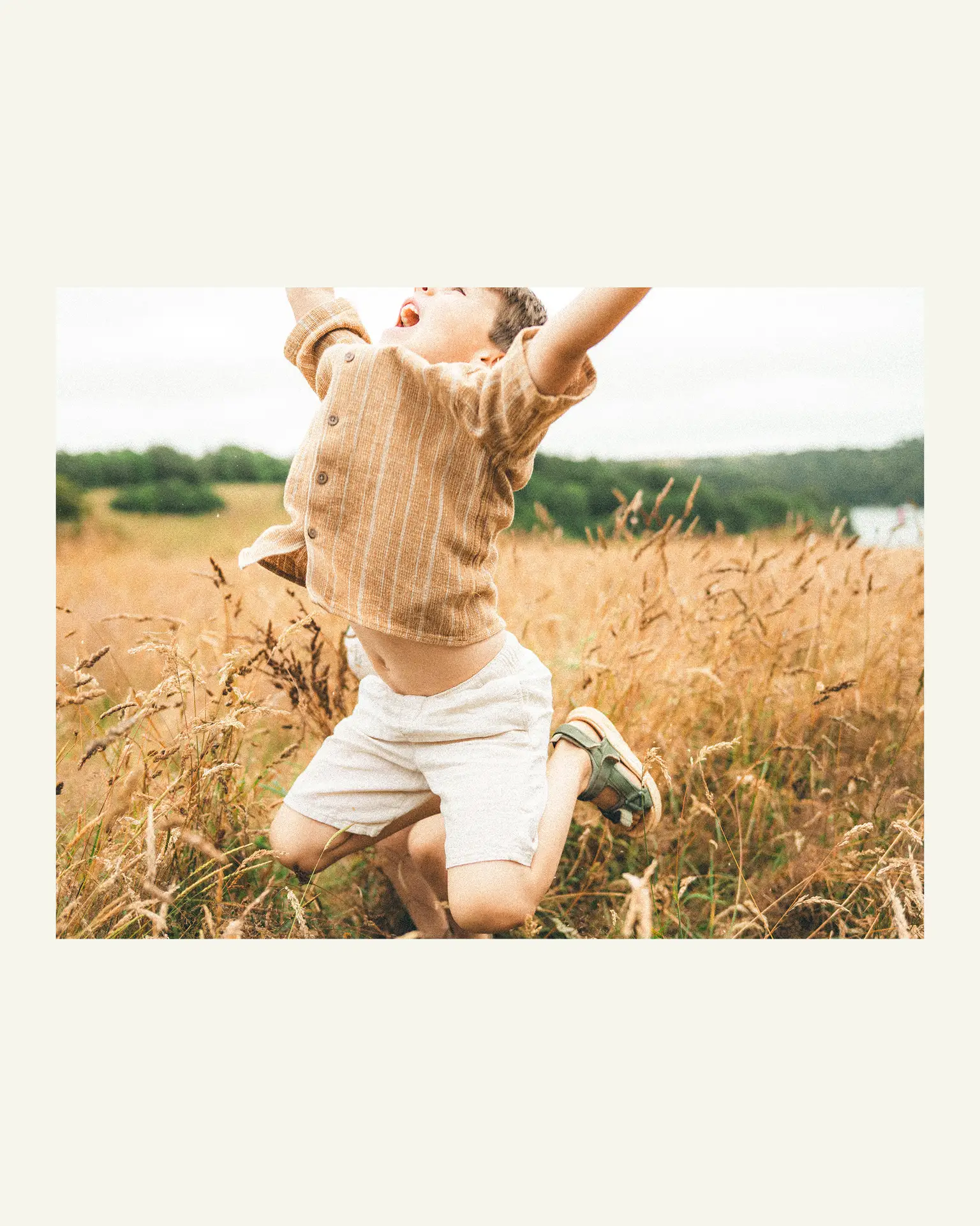 Young boy jumping with his arms raised in long grass beside the Fal Estuary at Trelissick Gardens