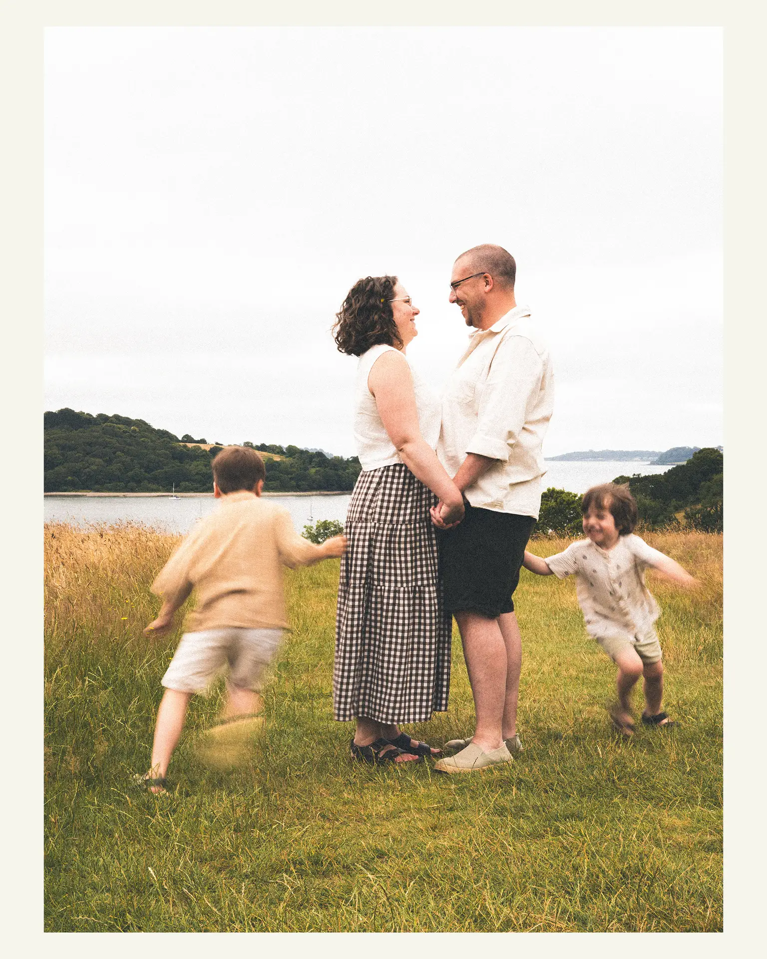 Parents holding hands while their two sons run around them during a family photoshoot at Trelissick Gardens