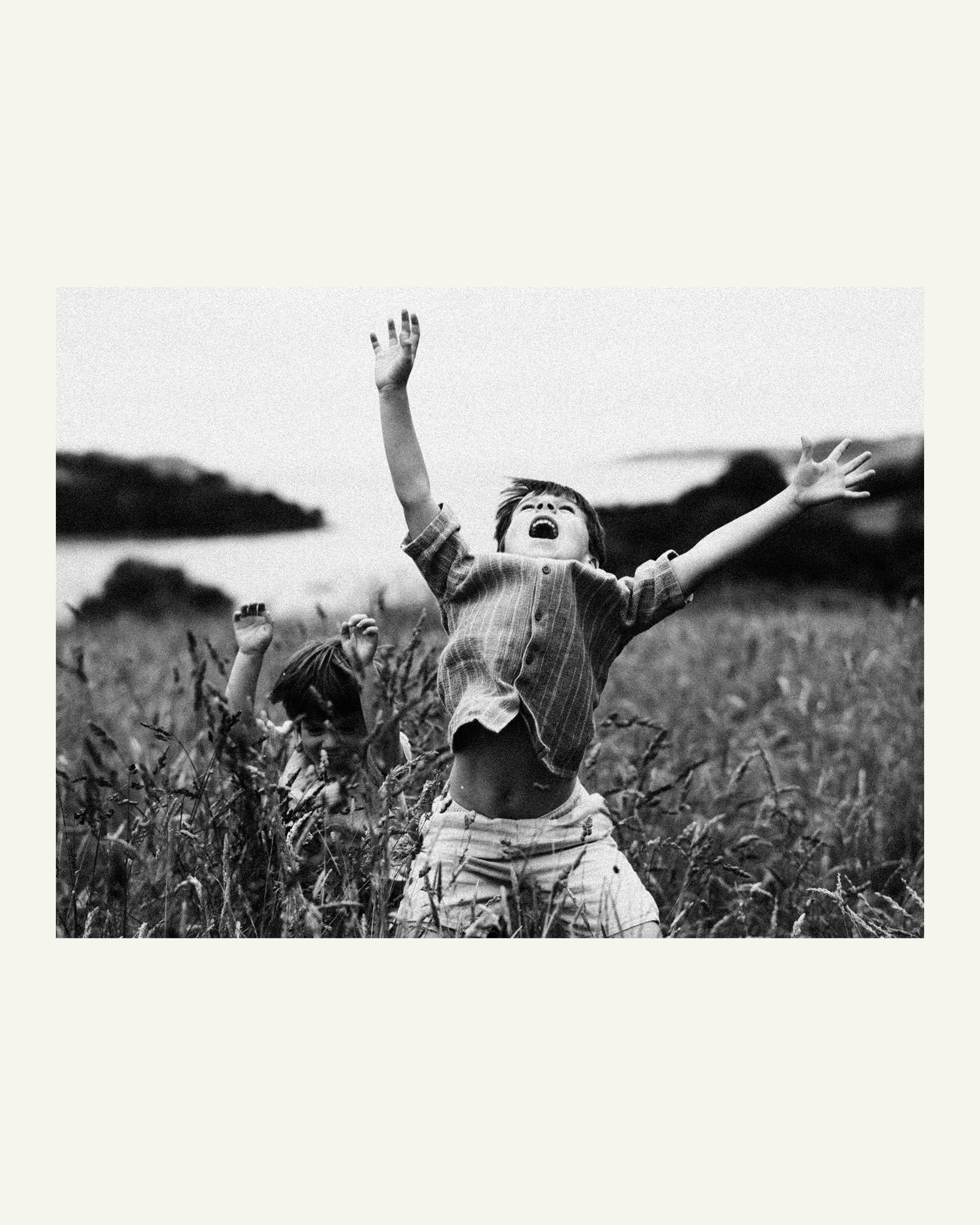 Two young brothers throwing their arms in the air while exploring a meadow at Trelissick Gardens