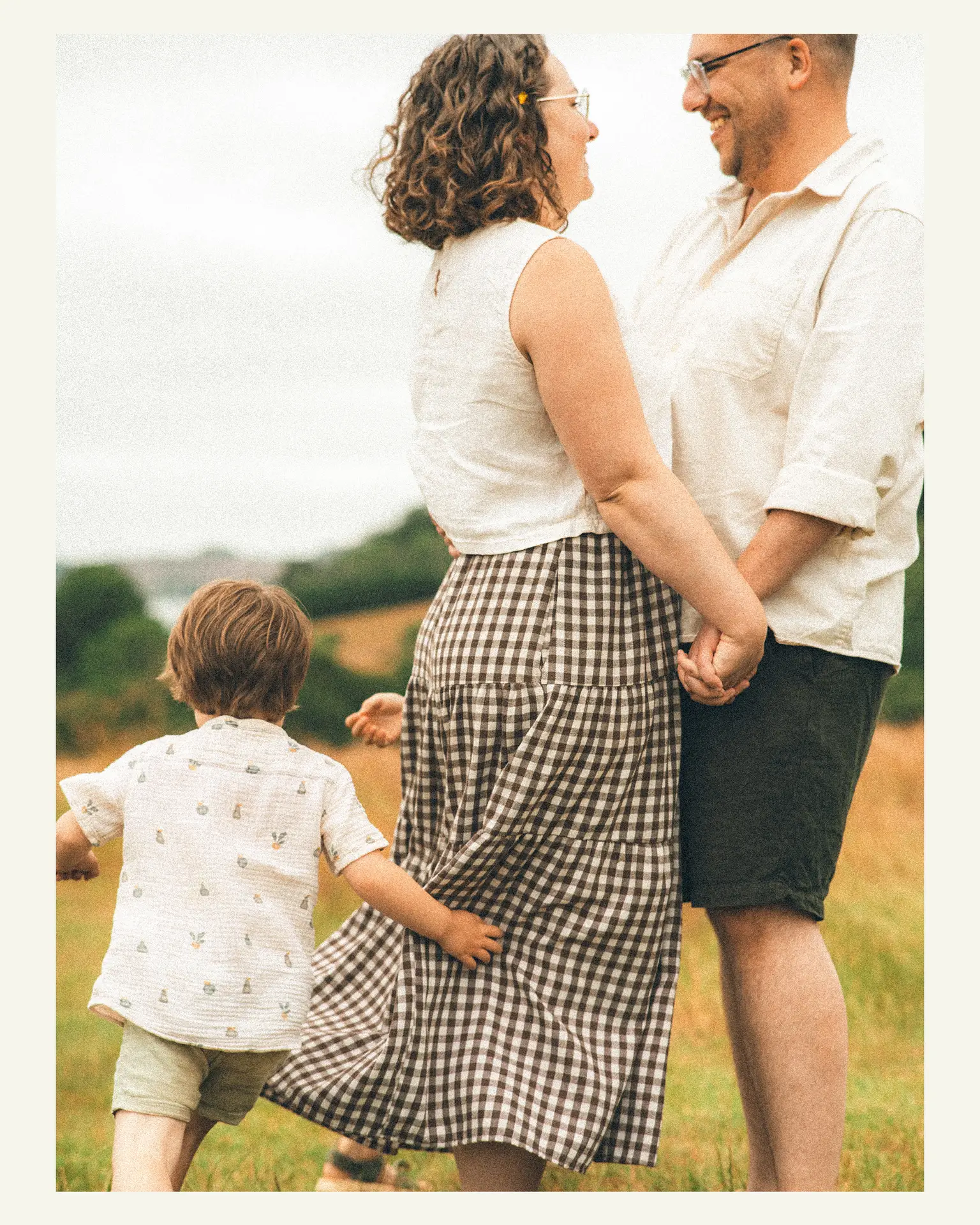 Young son hugging his mother as his parents smile together in a meadow at Trelissick Gardens