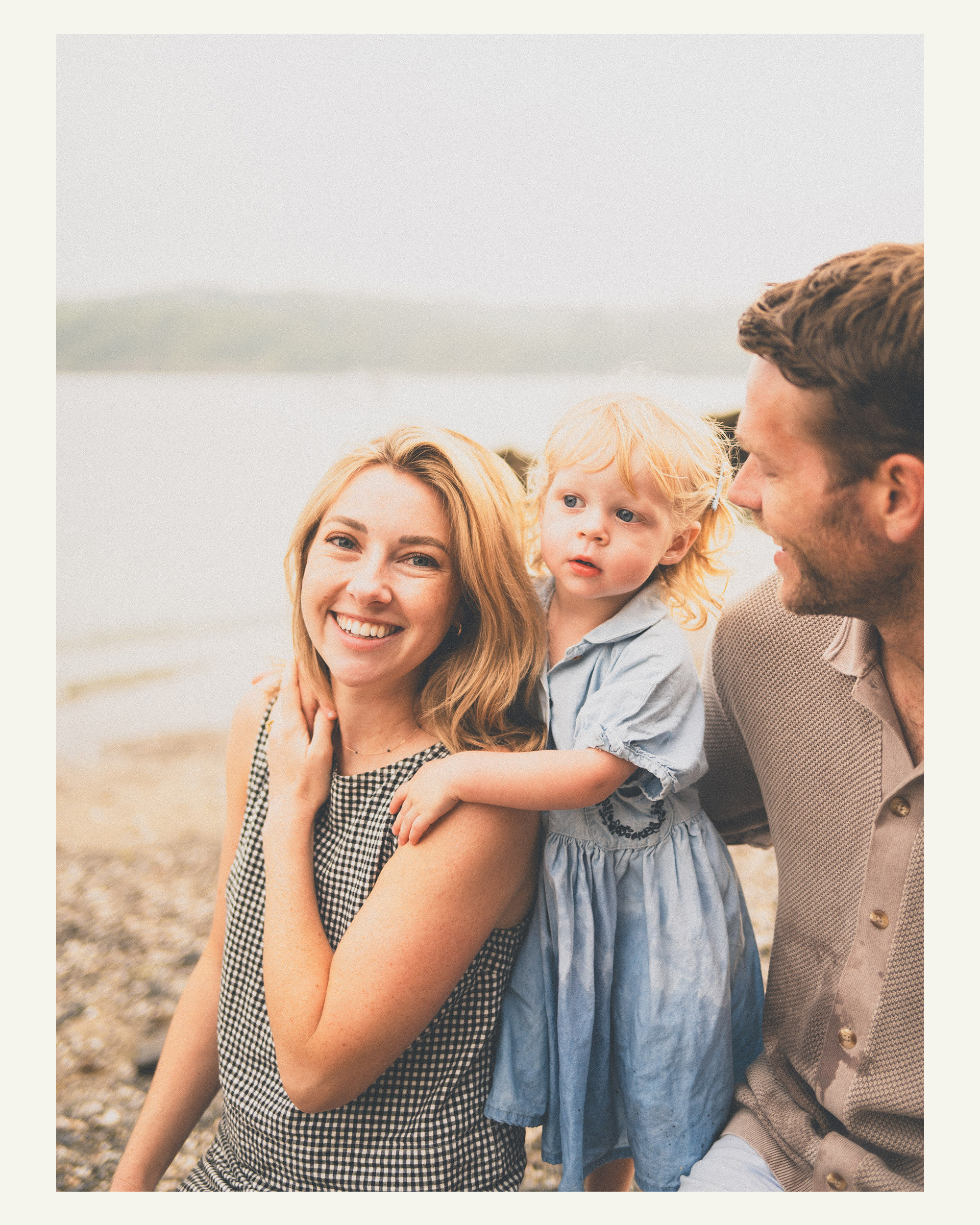 Parents sitting with their young daughter on the beach during a family photoshoot in Cornwall