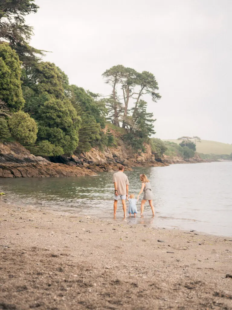 Parents holding their young daughter’s hands as they paddle at Grebe Beach near Falmouth