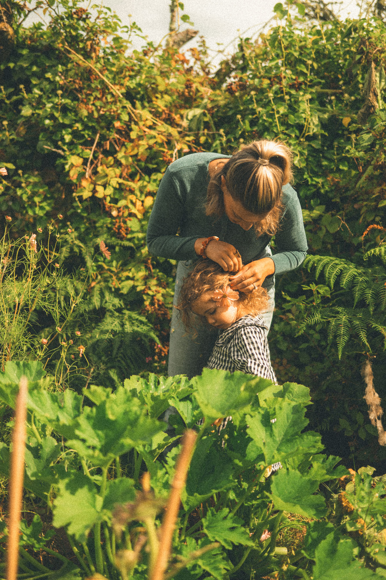 Mother gently placing a flower in her daughter's hair in their garden near St Ives