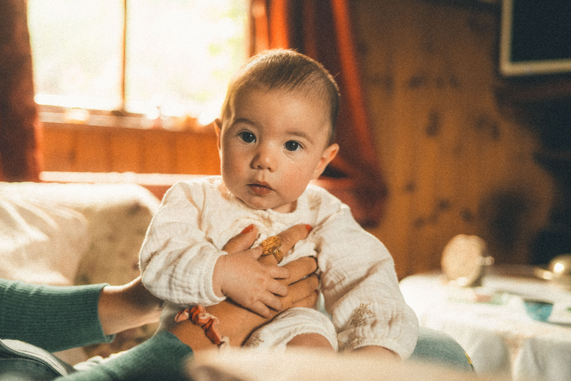 Baby sitting securely on their mother's lap in warm window light at home