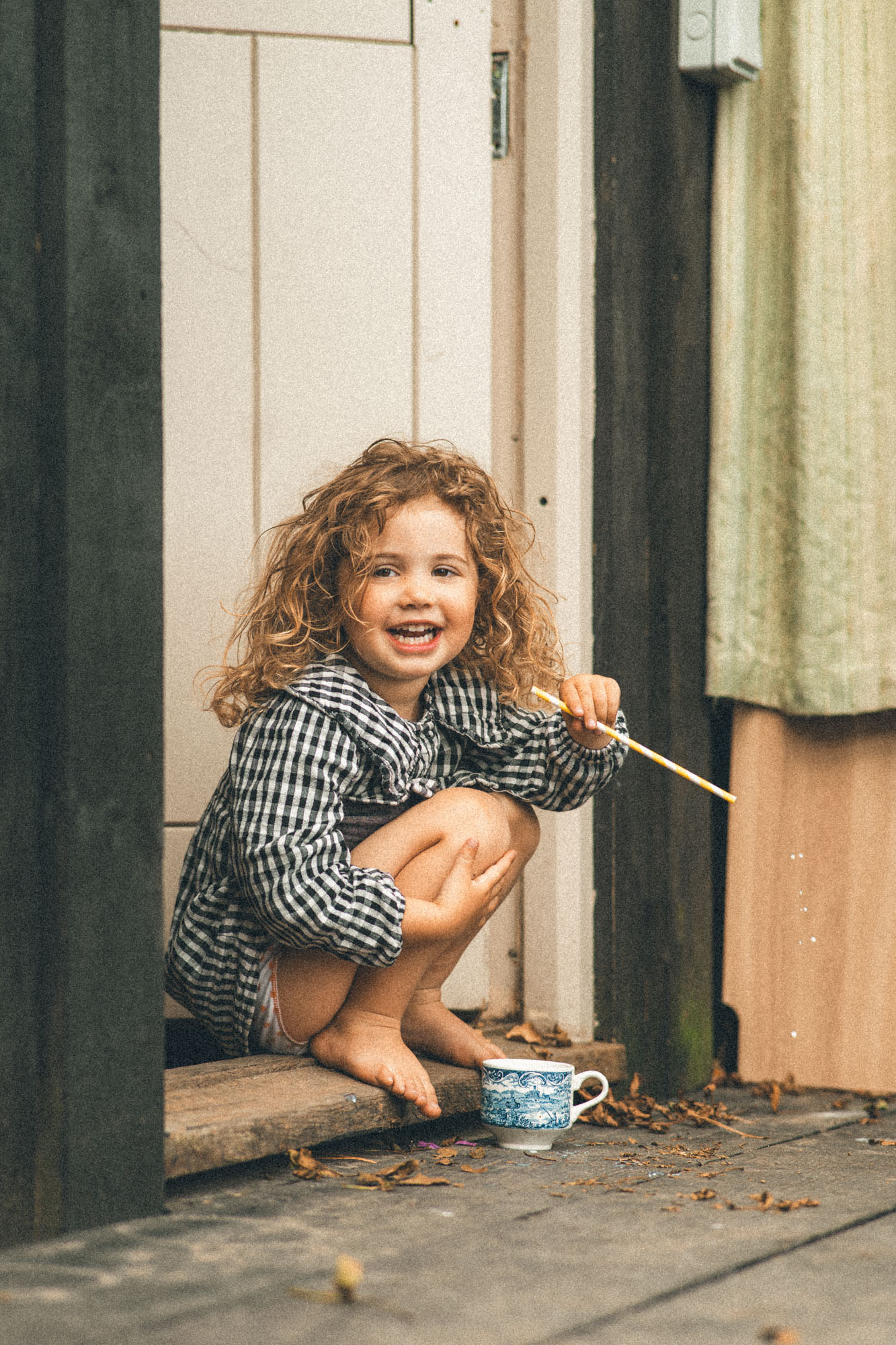 Smiling little girl with a teacup sitting on the doorstep of her family home