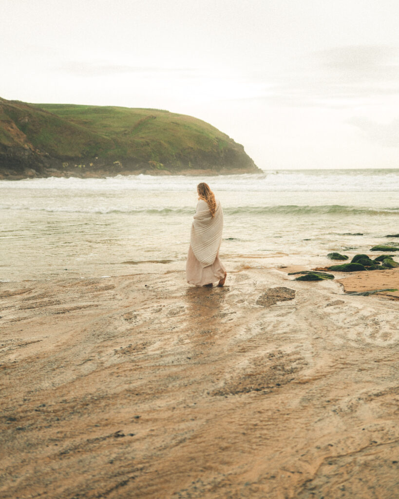 Expectant mother beside the waves at Poldhu Beach during an evening maternity photoshoot in Cornwall.