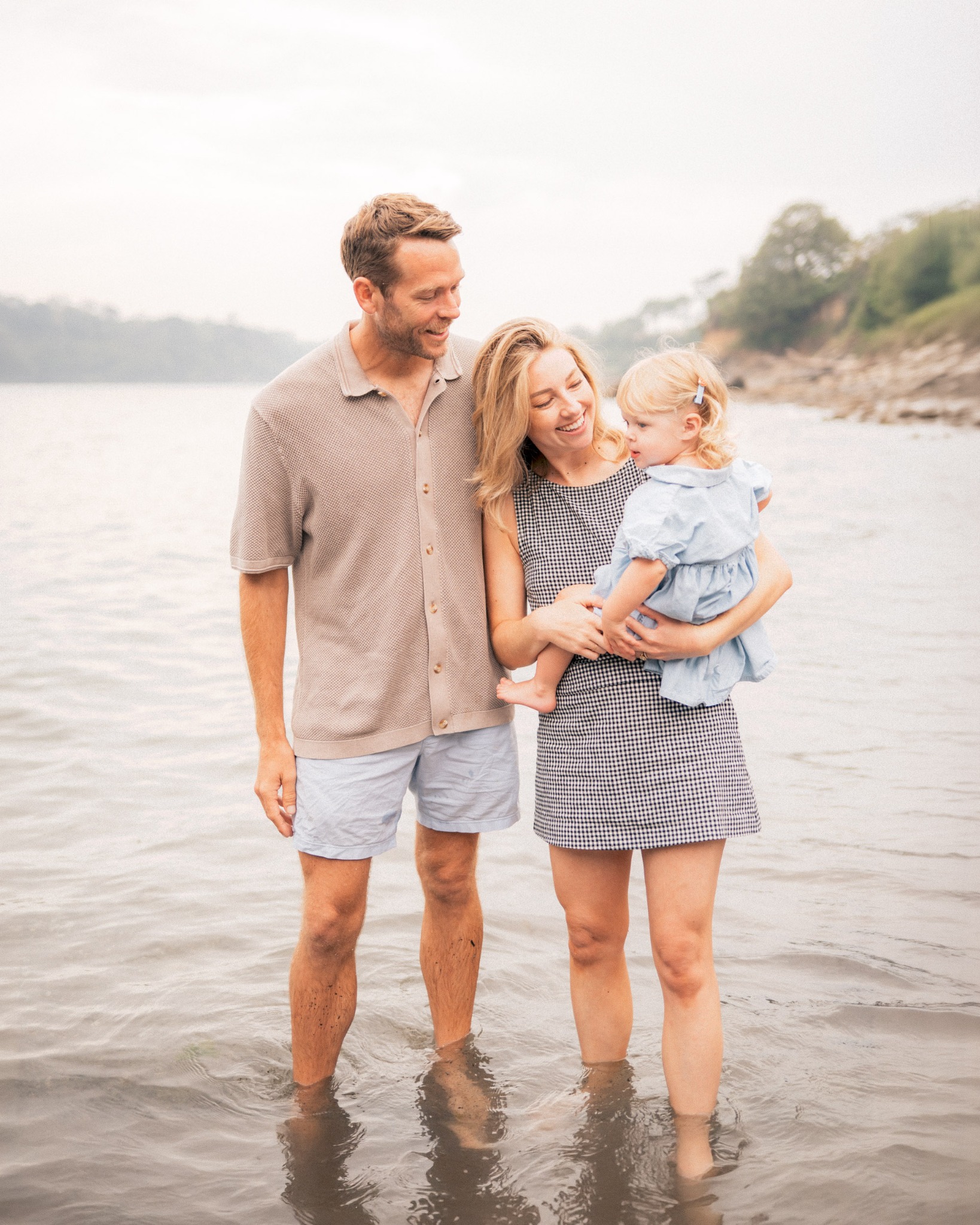 Parents smiling together with their young daughter in the shallow sea on a Cornish beach