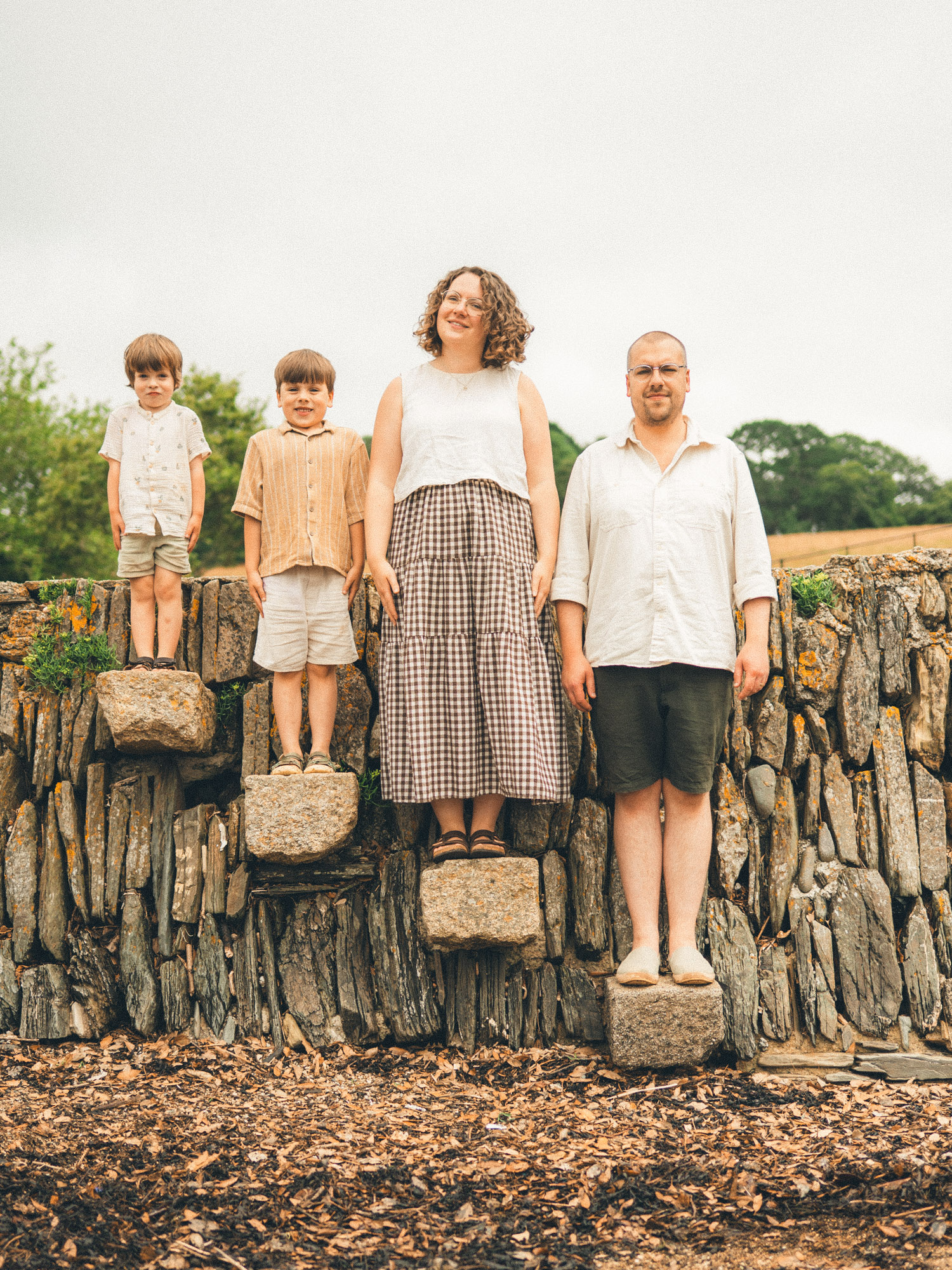 Family of four standing together on stones in front of a rustic stone wall