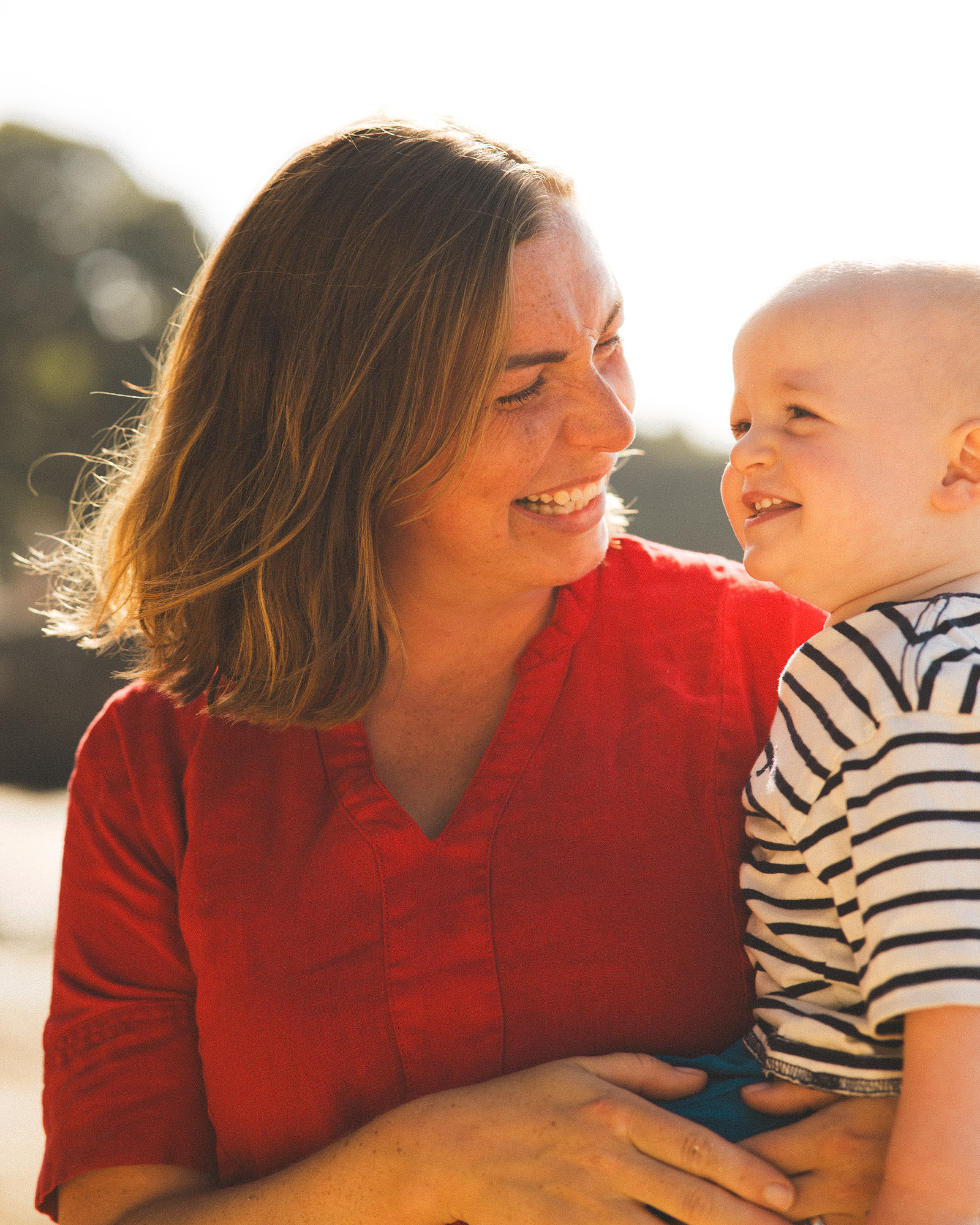 Mother in a red dress smiling at her young child outdoors